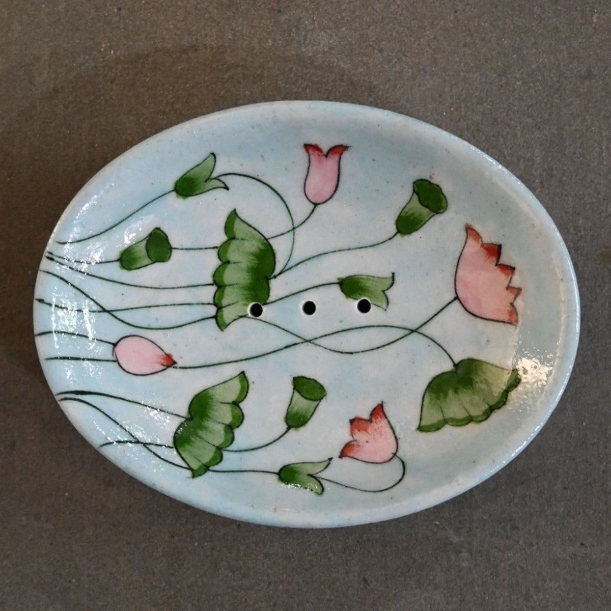 Oval ceramic light blue soap dish with a floral pink and green motif against a stone grey background 
