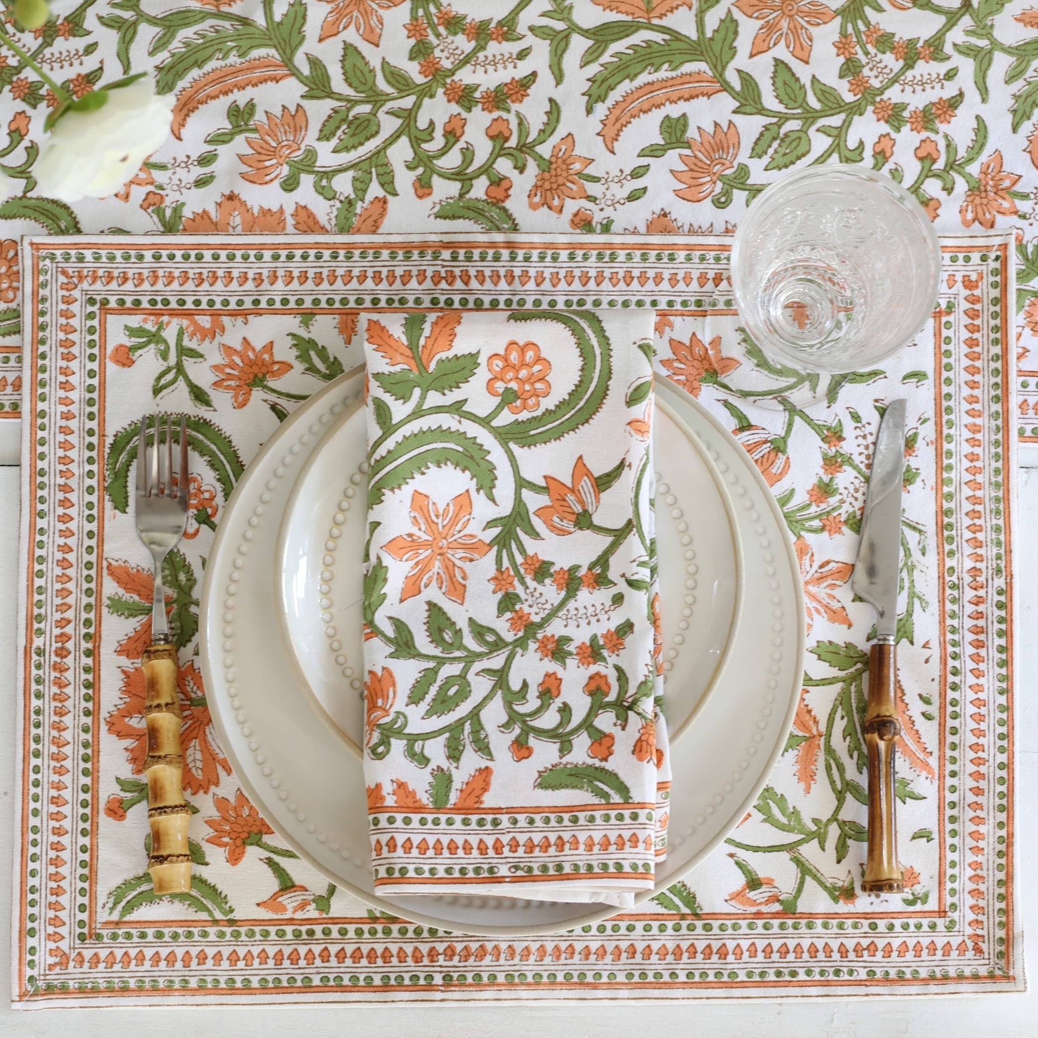 Decorative table setting with floral patterned placemat, plates, cutlery, and blockprinted cotton napkins in Orange Floral Vines motif.