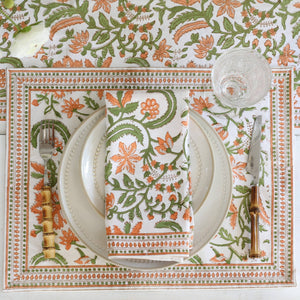 Decorative table setting with floral patterned placemat, plates, cutlery, and blockprinted cotton napkins in Orange Floral Vines motif.