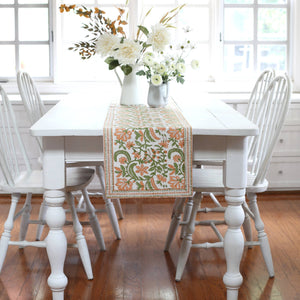 Dining room with white table and chairs, floral centerpiece, and decorative table runner, blockprinted, orange with floral vine motif.