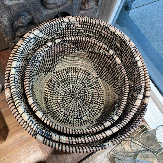 Round hold-all Woven baskets nested in each other in the shop window at Hill Station. Three baskets of different sizes, small, medium and large are nested each other.
