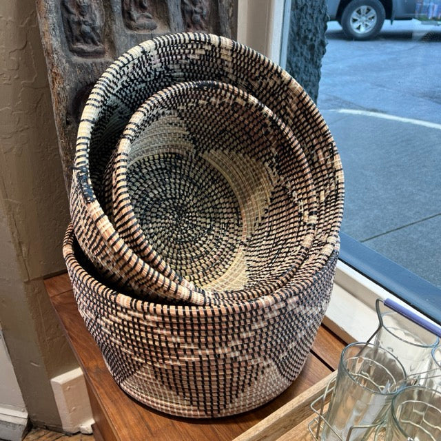 Stack of round hold-all Woven baskets in the shop window at Hill Station. Three baskets of different sizes, small, medium and large are stacked on each other.