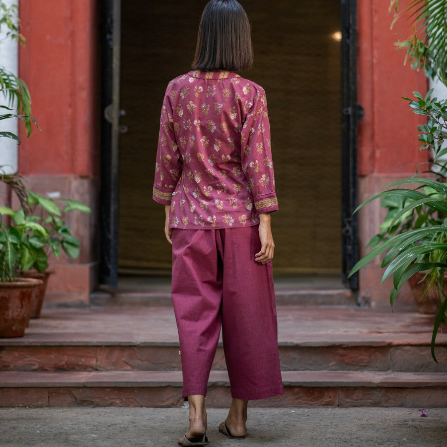 Woman in a pink outfit standing in front of a red building entrance, with her back turned to the camera