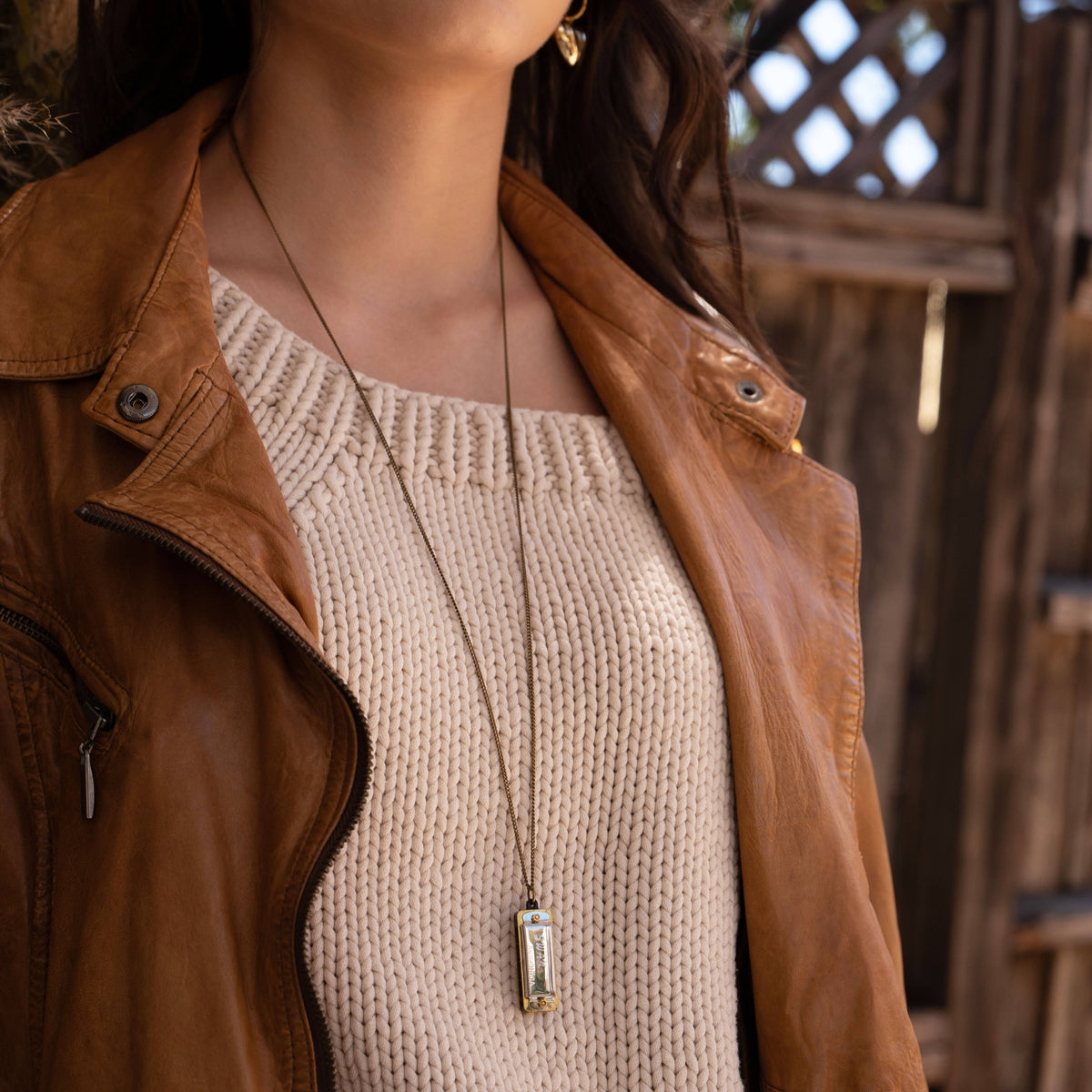 Mini vintage-style Swan harmonica pendant necklace worn by a woman wearing a cream knitted top and rust jacket , against a wooden background.