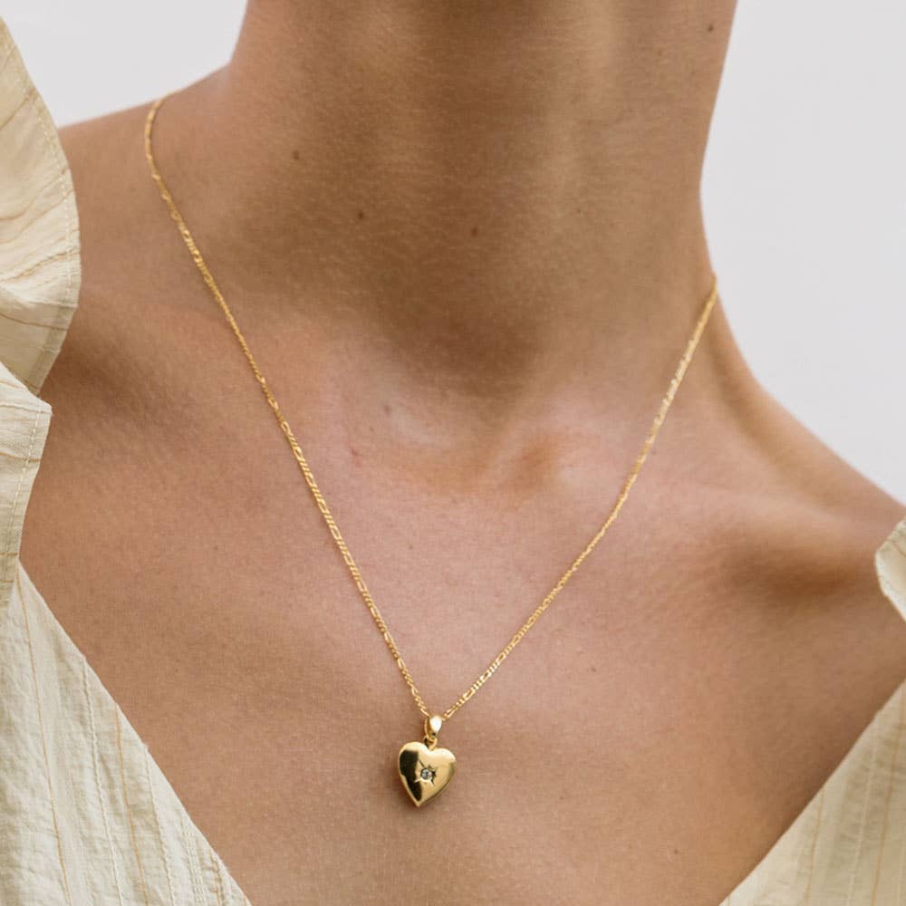 Gold heart locket necklace with Czech crystal and figaro chain being worn by a woman wearing a cream top